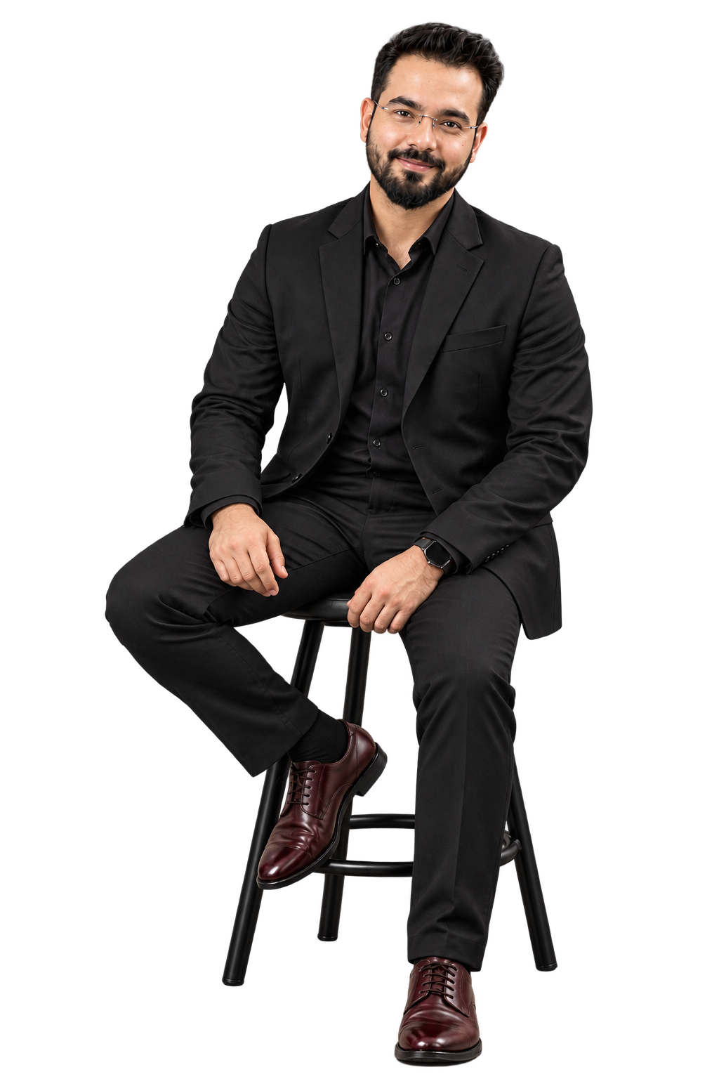 Professional portrait of a man in a black suit and shirt, seated on a stool, smiling at the camera against a dark studio background.